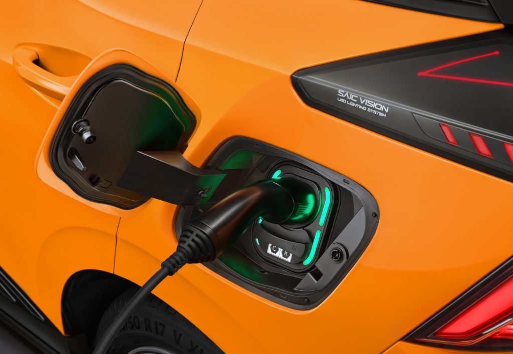 MG4 Electric in Orange lädt an einer Ladesäule. Detailansicht des CCS Combo 2 Ladeanschlusses mit eingestecktem Stecker und grüner LED-Beleuchtung.