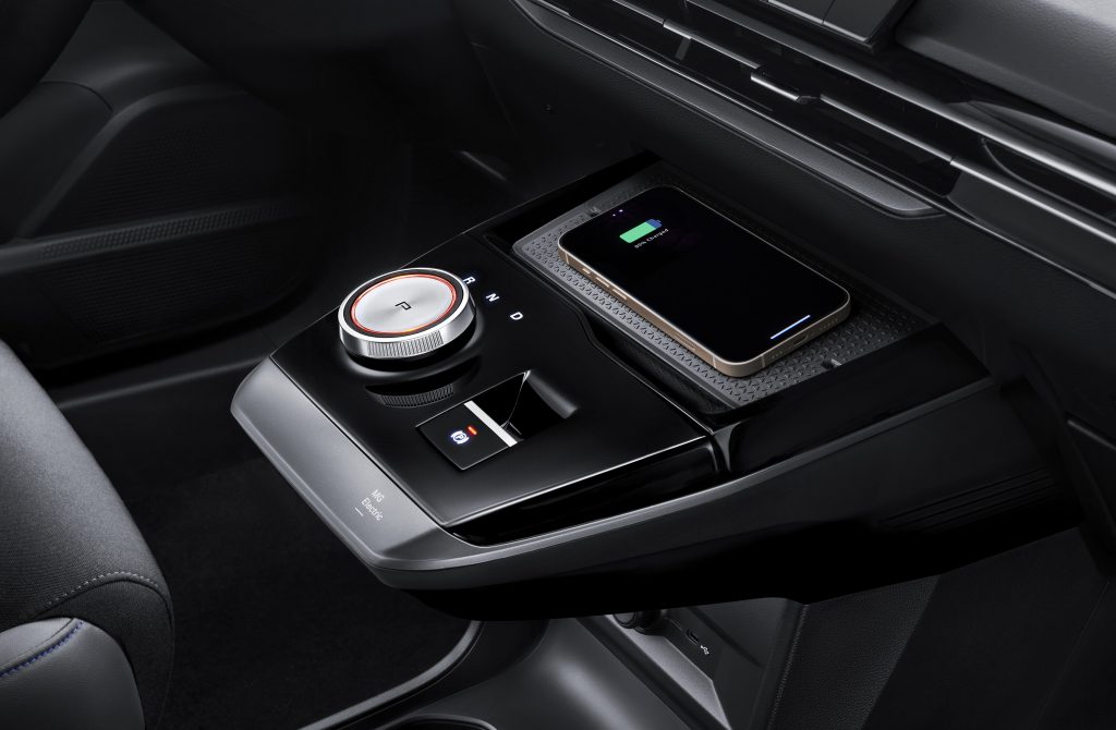 Gerne, hier sind die Vorschläge für das Bild der Mittelkonsole des MG4 mit Fokus auf das kabellose Laden und den Gangwahlschalter: Alttext (Alternativtext für Barrierefreiheit/SEO): Mittelkonsole des MG4 Electric mit dem runden Gangwahlschalter, einer Ablage und einem Smartphone, das kabellos (Wireless Charging) geladen wird.