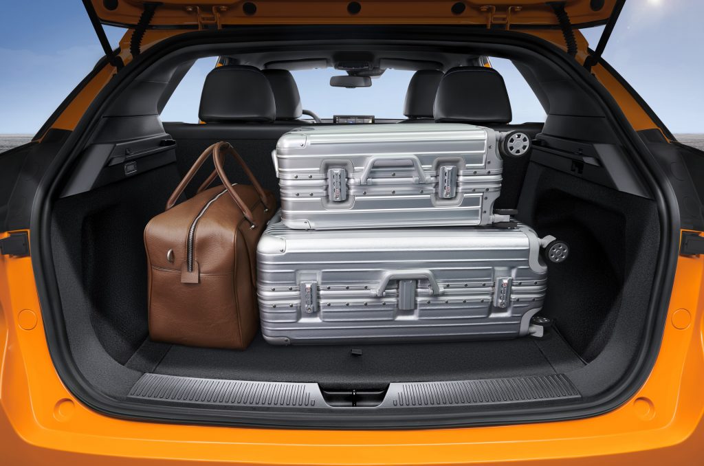 Kofferraum des orangefarbenen MG4 Electric mit gestapelten silbernen Koffern und einer braunen Reisetasche. Blick durch die geöffnete Heckklappe.