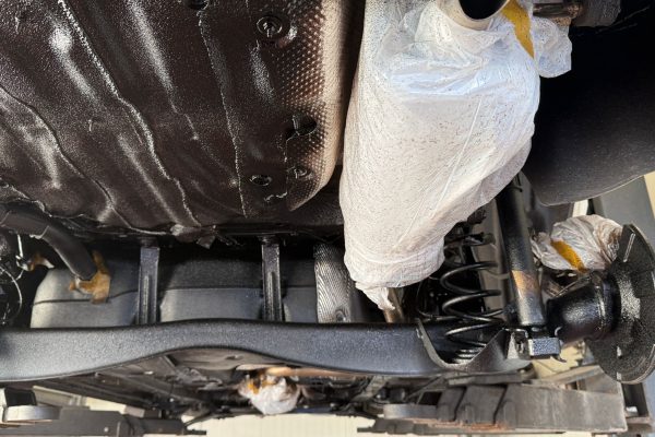 Elaskon Unterbodenaufbereitung – Detailansicht während der Konservierung Detailansicht des Fahrzeugunterbodens während der Elaskon Unterbodenaufbereitung mit abgeklemmter Abgasanlage und konservierten Fahrwerkskomponenten
