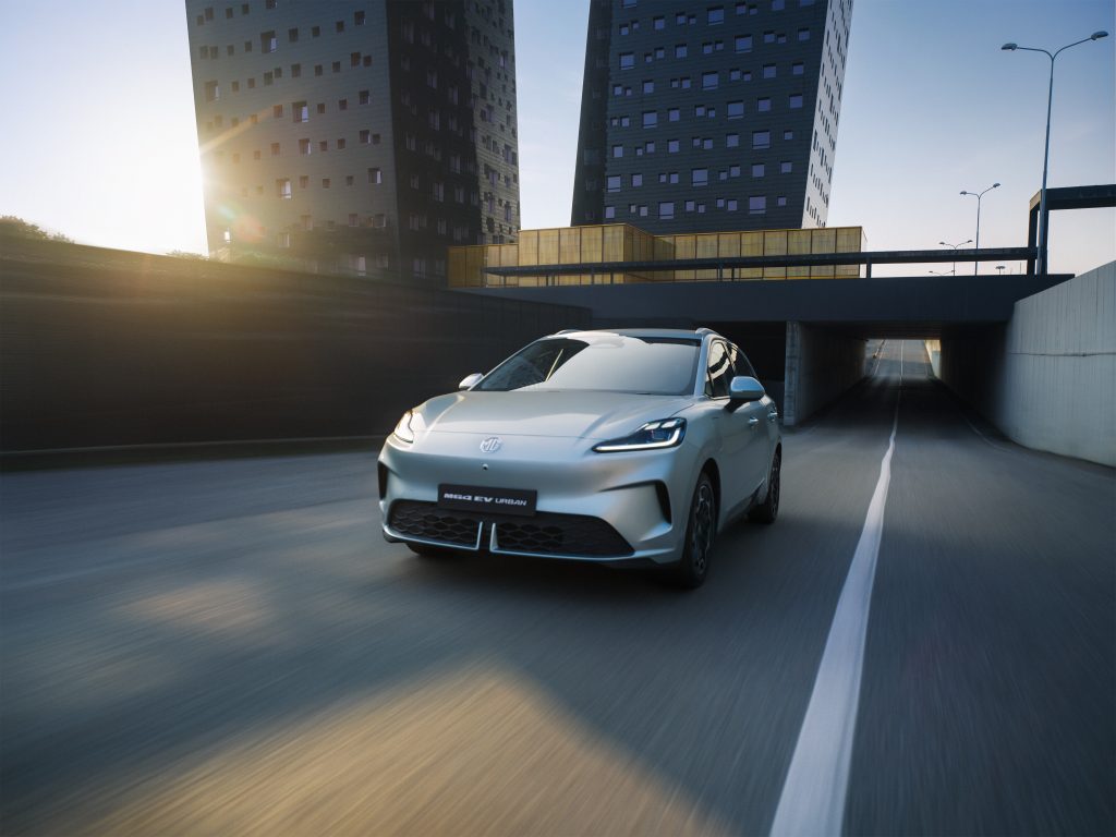 MG4 Urban Elektroauto fährt durch moderne Stadt bei Sonnenaufgang
